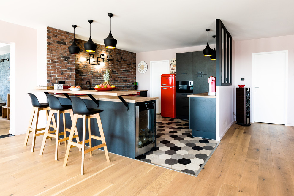 Photo of a contemporary eat-in kitchen in Montpellier with a single-bowl sink, wood benchtops, coloured appliances, ceramic floors, multi-coloured floor, black cabinets and brick splashback.