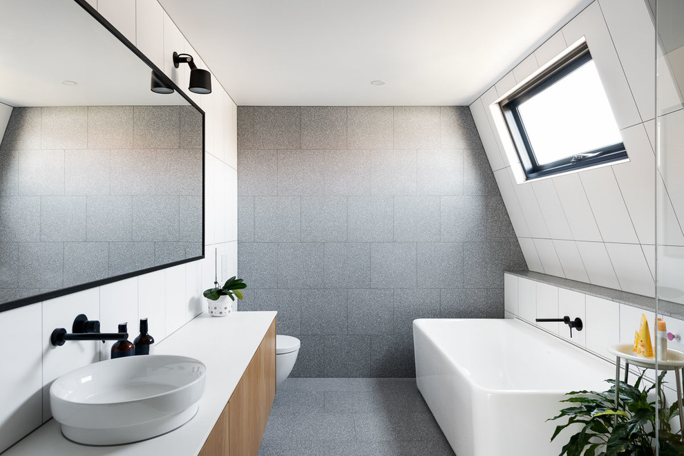 Inspiration for a mid-sized contemporary kids bathroom in Melbourne with flat-panel cabinets, a freestanding tub, gray tile, stone tile, white walls, concrete floors, engineered quartz benchtops, grey floor, white benchtops, medium wood cabinets and a vessel sink.