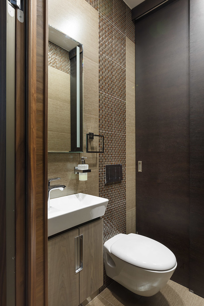 Design ideas for a mid-sized contemporary powder room in Saint Petersburg with a wall-mount toilet, brown tile, ceramic tile, brown walls, ceramic floors, flat-panel cabinets, light wood cabinets and a vessel sink.