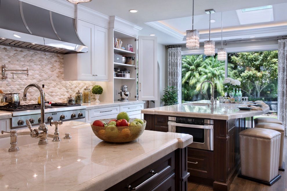This is an example of a large transitional galley eat-in kitchen in Orange County with multiple islands, an undermount sink, shaker cabinets, white cabinets, marble benchtops, beige splashback, mosaic tile splashback, stainless steel appliances and medium hardwood floors.