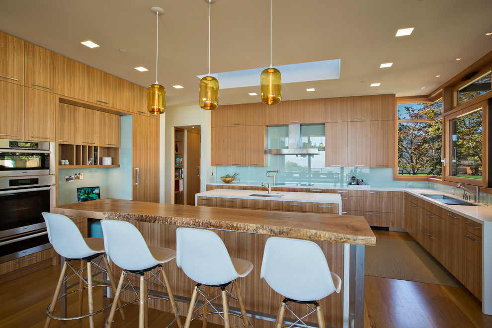Photo of a contemporary u-shaped kitchen in San Francisco with an undermount sink, flat-panel cabinets, medium wood cabinets, glass sheet splashback, stainless steel appliances, medium hardwood floors and multiple islands.