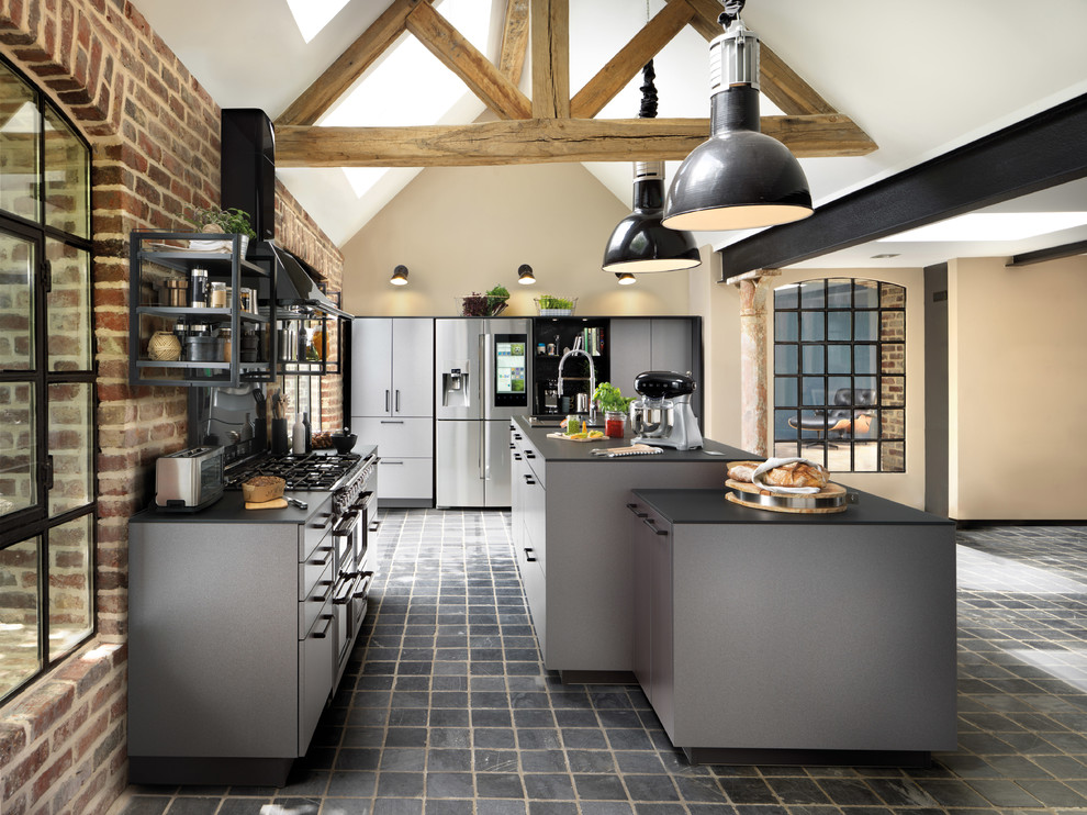 Design ideas for a large industrial single-wall open plan kitchen in Surrey with a single-bowl sink, flat-panel cabinets, laminate benchtops, black appliances, slate floors, with island, black floor and black benchtop.