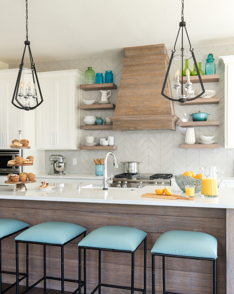 Design ideas for a mid-sized beach style l-shaped open plan kitchen with a farmhouse sink, shaker cabinets, white cabinets, quartz benchtops, grey splashback, ceramic splashback, stainless steel appliances, medium hardwood floors, with island and brown floor.