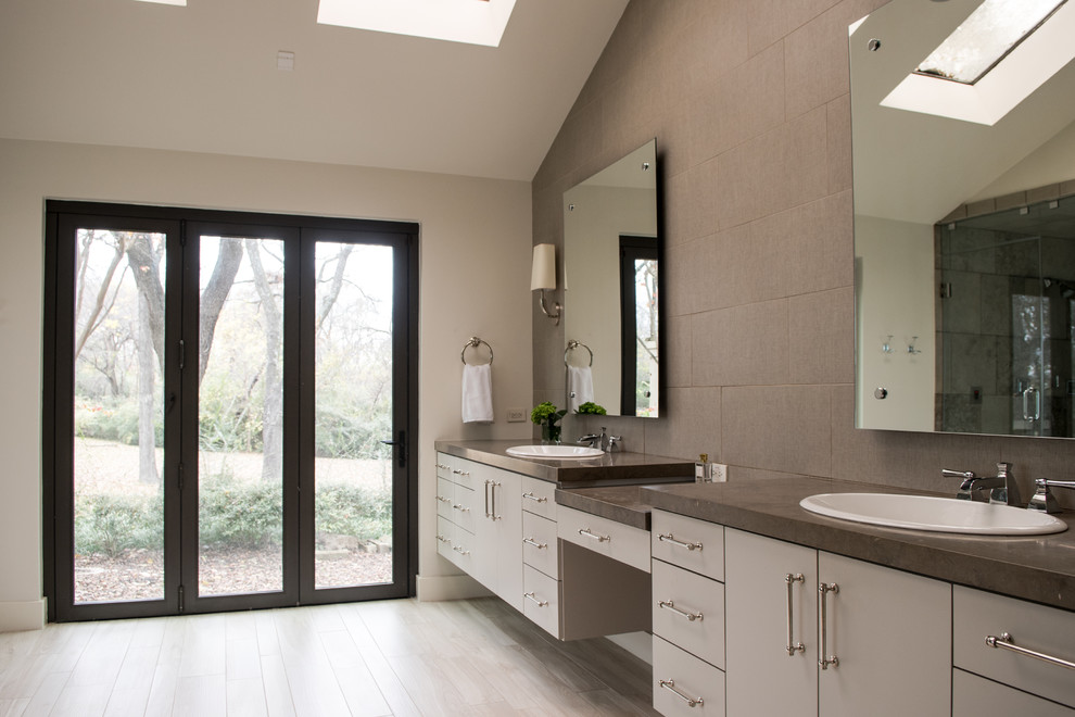 Inspiration for a mid-sized transitional master gray tile and cement tile light wood floor and beige floor drop-in bathtub remodel in Dallas with flat-panel cabinets, gray cabinets, gray walls, a drop-in sink, concrete countertops and a hinged shower door