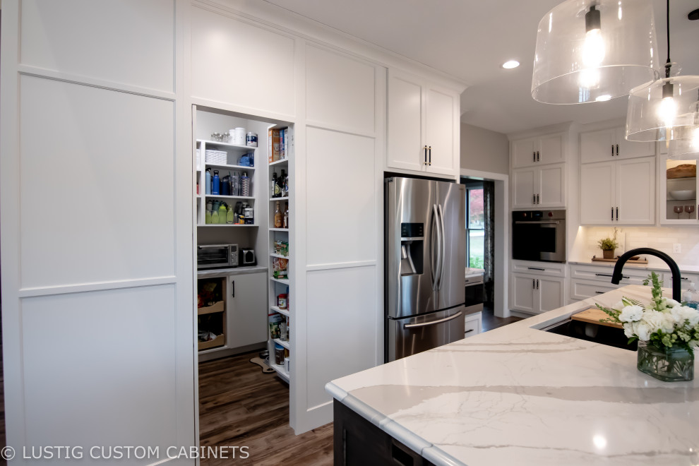 Inspiration for a large transitional l-shaped laminate floor and brown floor open concept kitchen remodel with an undermount sink, flat-panel cabinets, white cabinets, quartz countertops, white backsplash, ceramic backsplash, stainless steel appliances, an island and white countertops