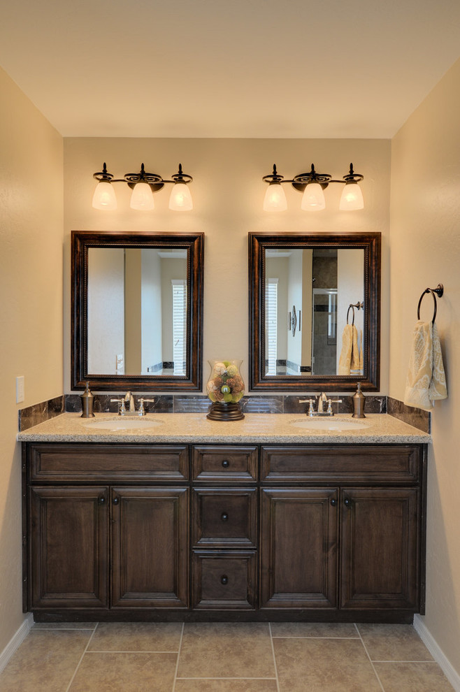 Mediterranean master bathroom in Phoenix with an undermount sink, recessed-panel cabinets, dark wood cabinets, granite benchtops, brown tile, porcelain tile, brown walls and porcelain floors.