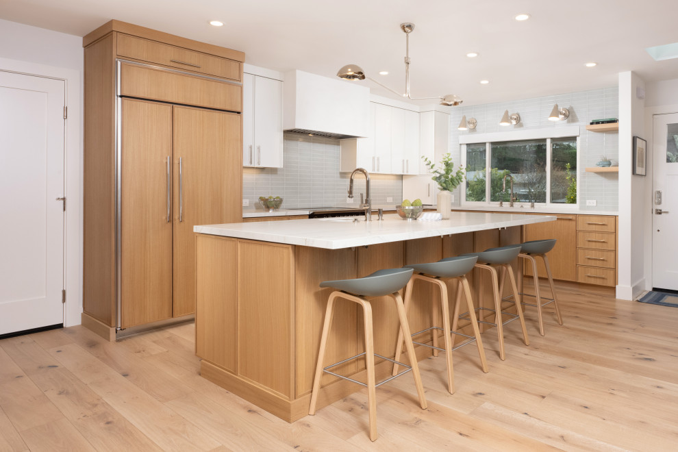 Inspiration for a large contemporary l-shaped open plan kitchen in San Francisco with a submerged sink, shaker cabinets, light wood cabinets, engineered stone countertops, green splashback, ceramic splashback, integrated appliances, light hardwood flooring, an island, brown floors and white worktops.