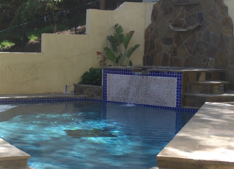 Design ideas for a mid-sized traditional backyard custom-shaped lap pool in Los Angeles with natural stone pavers and a water feature.