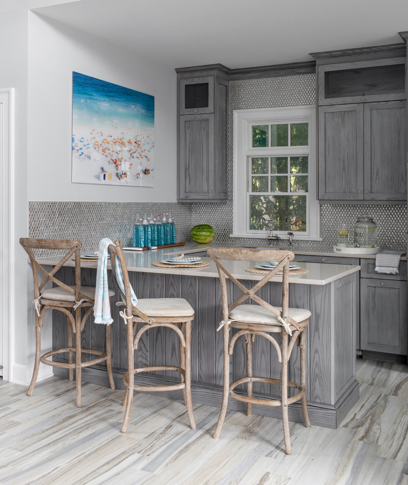 Inspiration for a beach style u-shaped home bar in New York with shaker cabinets, grey cabinets, metal splashback, beige floor and beige benchtop.