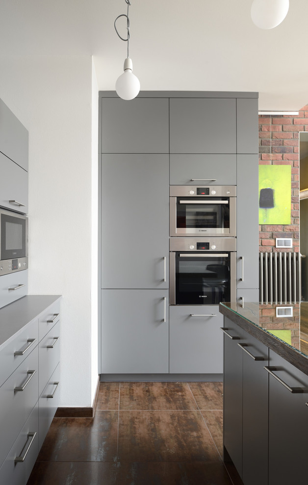 Photo of a mid-sized industrial u-shaped separate kitchen in Other with an integrated sink, flat-panel cabinets, grey cabinets, granite benchtops, orange splashback, glass sheet splashback, stainless steel appliances, ceramic floors and with island.