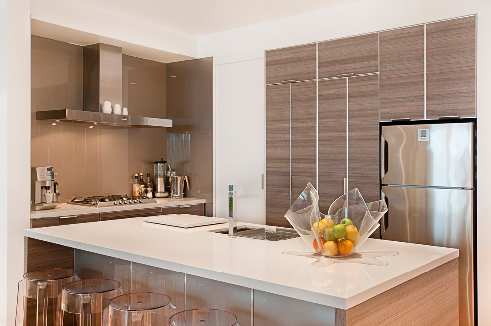 This is an example of a mid-sized contemporary l-shaped open plan kitchen in Melbourne with an undermount sink, flat-panel cabinets, medium wood cabinets, quartz benchtops, beige splashback, glass tile splashback, stainless steel appliances, light hardwood floors and with island.