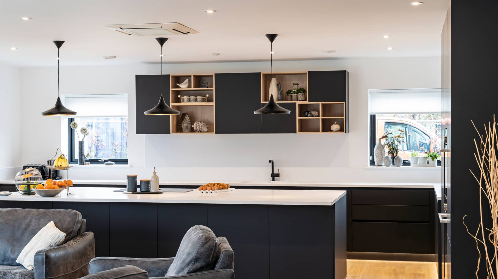 Large modern single-wall open plan kitchen in Oxfordshire with a drop-in sink, flat-panel cabinets, black cabinets, quartzite benchtops, white splashback, with island and white benchtop.