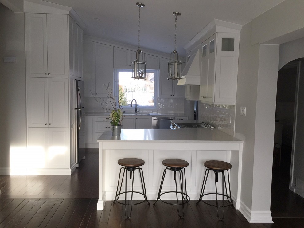 Small transitional u-shaped medium tone wood floor and brown floor kitchen photo in Toronto with flat-panel cabinets, white cabinets, quartz countertops, white backsplash, ceramic backsplash, stainless steel appliances and a peninsula