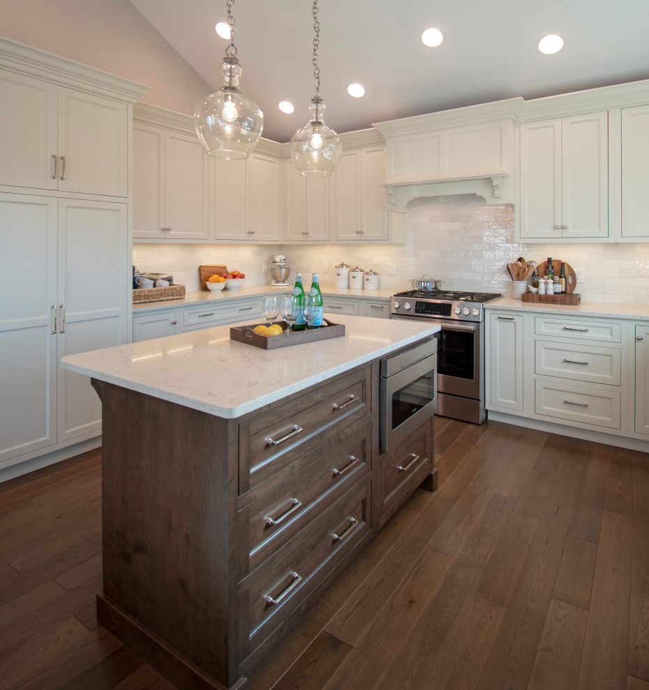 Inspiration for a transitional medium tone wood floor, brown floor and vaulted ceiling eat-in kitchen remodel with shaker cabinets, white cabinets, quartz countertops, white backsplash, ceramic backsplash, stainless steel appliances, an island and white countertops