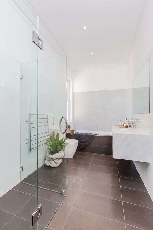 This is an example of a contemporary bathroom in Adelaide with white tile, ceramic tile, white walls, porcelain floors, quartzite benchtops, brown floor, a drop-in sink and white benchtops.