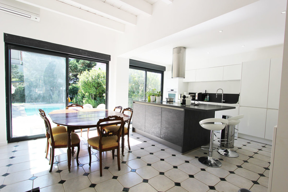 This is an example of a large eclectic galley eat-in kitchen in Lyon with an undermount sink, flat-panel cabinets, white cabinets, black splashback, slate splashback, stainless steel appliances, marble floors, with island, multi-coloured floor and black benchtop.