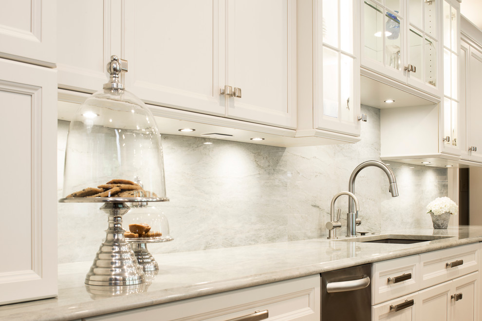 Large transitional single-wall medium tone wood floor and brown floor kitchen photo in Denver with an undermount sink, recessed-panel cabinets, white cabinets, white backsplash, stone slab backsplash, stainless steel appliances and an island