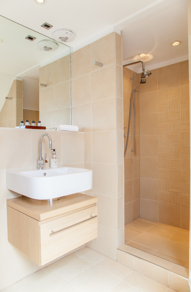 This is an example of a transitional bathroom in Edinburgh with a wall-mount sink, flat-panel cabinets, light wood cabinets, an alcove shower, beige tile, ceramic tile, beige walls and ceramic floors.