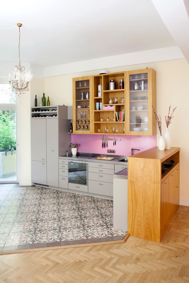 Expansive contemporary l-shaped open plan kitchen in Cologne with an integrated sink, flat-panel cabinets, grey cabinets, stainless steel benchtops, pink splashback, timber splashback, cement tiles, multi-coloured floor and grey benchtop.