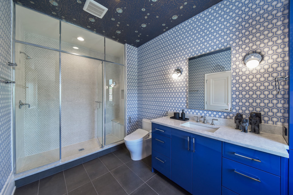 This is an example of a large eclectic kids bathroom in Chicago with flat-panel cabinets, blue cabinets, an alcove shower, a two-piece toilet, white tile, mosaic tile, blue walls, porcelain floors, an undermount sink, engineered quartz benchtops, grey floor, a hinged shower door, grey benchtops, a shower seat, a single vanity, a built-in vanity, wallpaper and wallpaper.