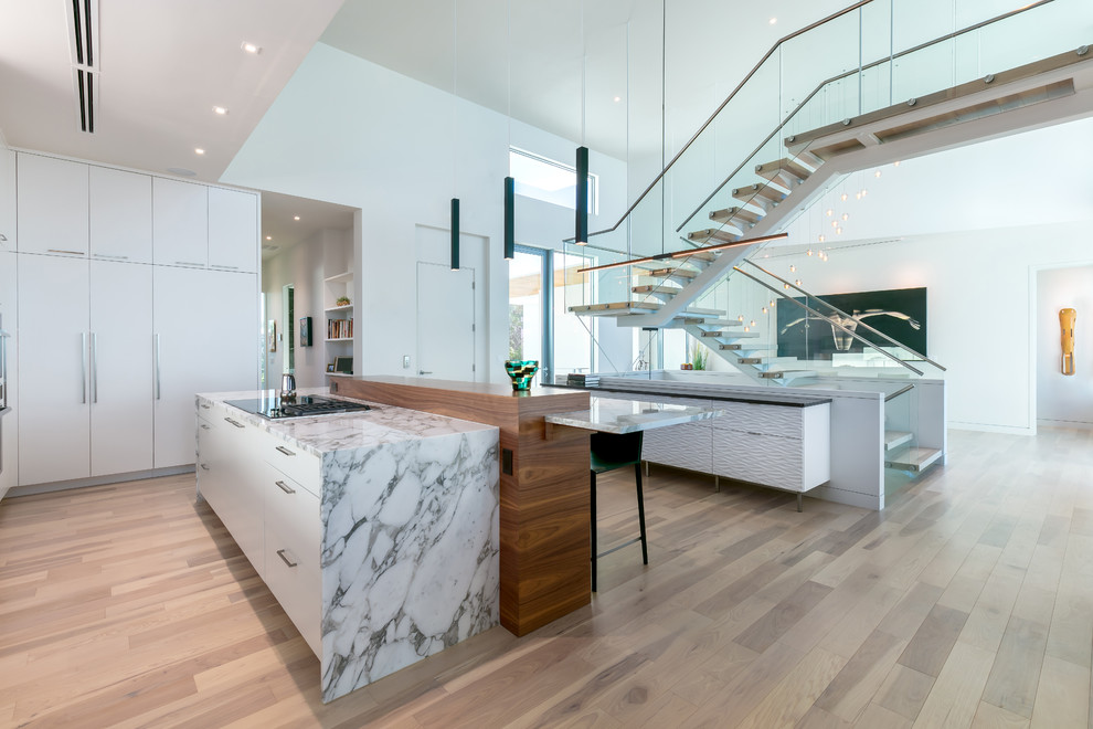 This is an example of a large contemporary l-shaped open plan kitchen in Tampa with a triple-bowl sink, flat-panel cabinets, white cabinets, quartzite benchtops, white splashback, window splashback, panelled appliances, light hardwood floors, with island and multi-coloured floor.
