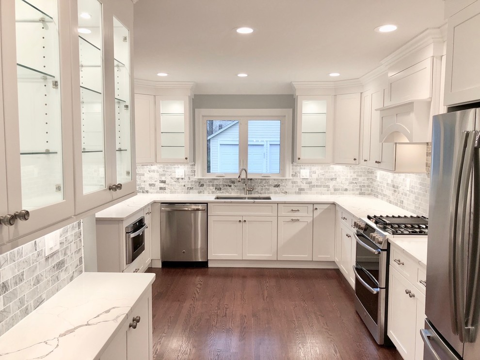 Inspiration for a mid-sized transitional u-shaped dark wood floor and brown floor enclosed kitchen remodel with an undermount sink, shaker cabinets, white cabinets, marble countertops, gray backsplash, stone tile backsplash, stainless steel appliances, no island and white countertops