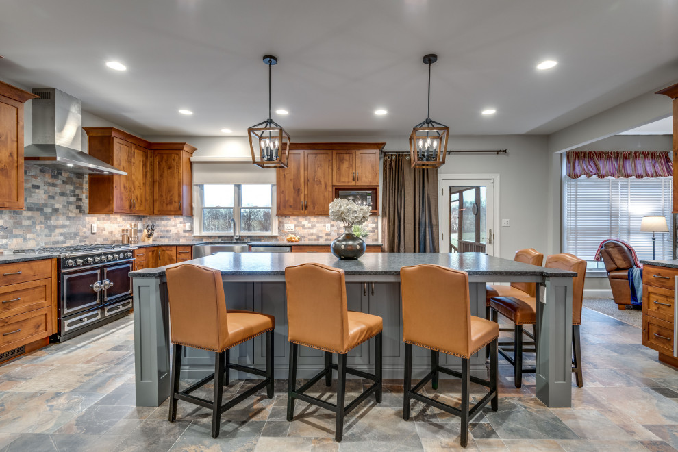 This is an example of an expansive country l-shaped kitchen in DC Metro with a farmhouse sink, shaker cabinets, granite benchtops, with island, medium wood cabinets, multi-coloured splashback, black appliances, multi-coloured floor and black benchtop.