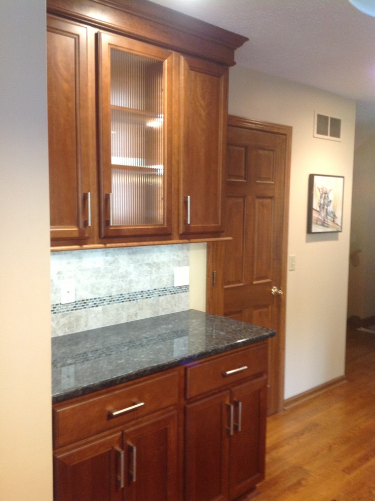Example of a mid-sized transitional l-shaped medium tone wood floor eat-in kitchen design with an undermount sink, recessed-panel cabinets, medium tone wood cabinets, granite countertops, gray backsplash, stone tile backsplash, stainless steel appliances, gray walls and an island