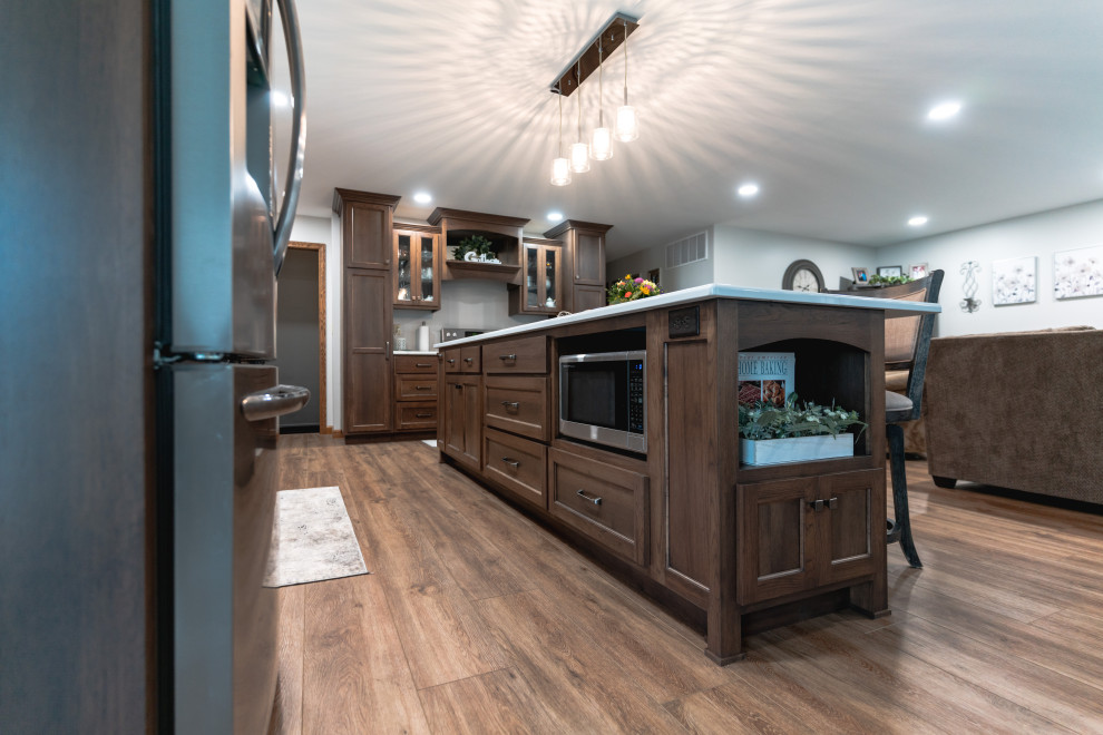 Open concept kitchen - huge transitional l-shaped medium tone wood floor and brown floor open concept kitchen idea with shaker cabinets, medium tone wood cabinets, quartz countertops, stainless steel appliances, an island and white countertops