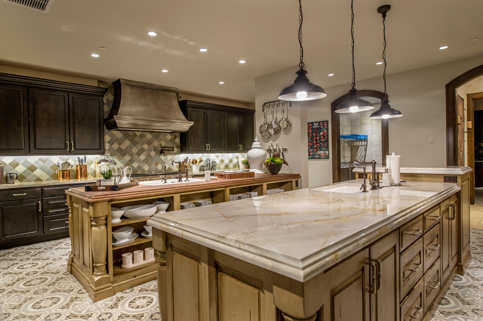 This is an example of an expansive country u-shaped separate kitchen in Denver with multiple islands, an undermount sink, raised-panel cabinets, distressed cabinets, soapstone benchtops, multi-coloured splashback, mosaic tile splashback, stainless steel appliances, vinyl floors and multi-coloured floor.