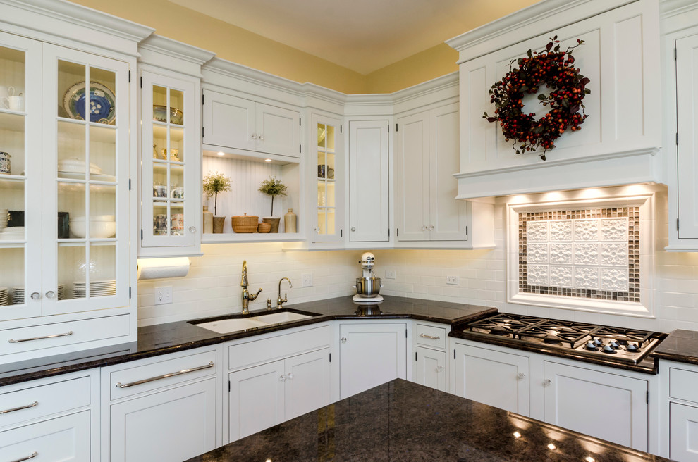 Large transitional l-shaped medium tone wood floor open concept kitchen photo in Chicago with a drop-in sink, glass-front cabinets, white cabinets, granite countertops, white backsplash, ceramic backsplash, stainless steel appliances and an island