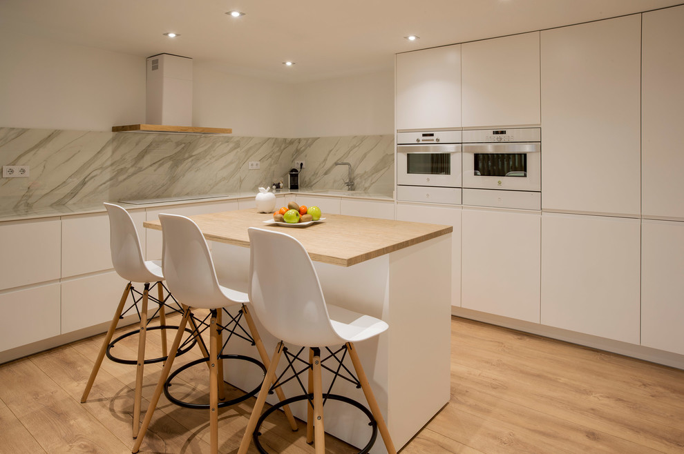 L-shaped kitchen in Barcelona with flat-panel cabinets, white cabinets, with island, an undermount sink, wood benchtops, grey splashback, white appliances, light hardwood floors, brown floor and beige benchtop.