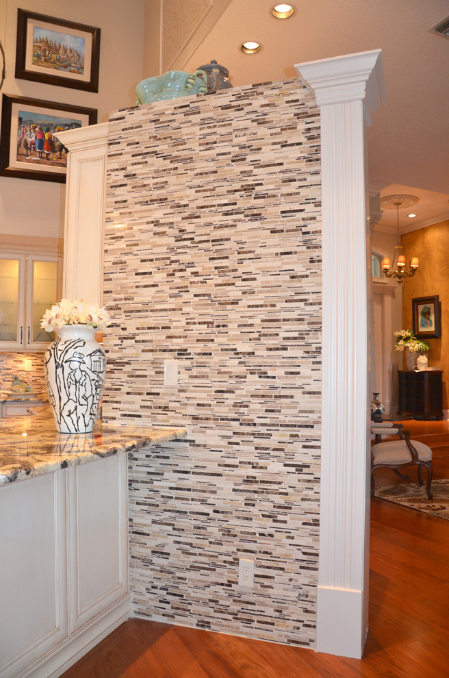 Inspiration for a large transitional medium tone wood floor open concept kitchen remodel in Miami with a farmhouse sink, glass-front cabinets, white cabinets, granite countertops, multicolored backsplash, custom tile backsplash, paneled appliances, beige walls and an island