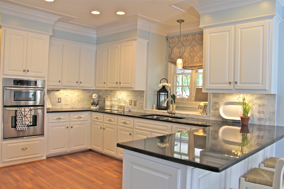 Example of a mid-sized beach style u-shaped medium tone wood floor kitchen design with raised-panel cabinets, white cabinets, granite countertops, white backsplash, subway tile backsplash, stainless steel appliances and an undermount sink