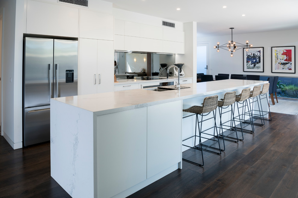 Photo of a contemporary kitchen in Melbourne with flat-panel cabinets, white cabinets, mirror splashback, stainless steel appliances, dark hardwood floors, with island, brown floor and white benchtop.