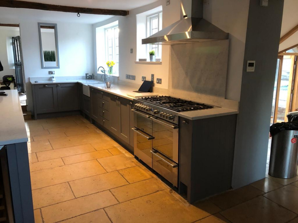 Photo of a large country l-shaped open plan kitchen in West Midlands with a farmhouse sink, shaker cabinets, grey cabinets, quartzite benchtops, black appliances, limestone floors, with island, beige floor and white benchtop.