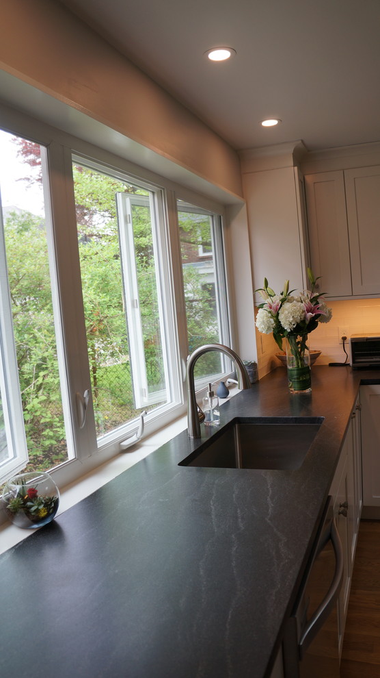 Inspiration for a mid-sized transitional l-shaped medium tone wood floor and brown floor open concept kitchen remodel in Boston with a single-bowl sink, shaker cabinets, white cabinets, granite countertops, white backsplash, window backsplash, stainless steel appliances, an island and black countertops