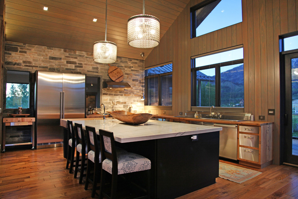 Open concept kitchen - mid-sized contemporary l-shaped medium tone wood floor and brown floor open concept kitchen idea with a drop-in sink, flat-panel cabinets, stainless steel cabinets, quartzite countertops, stainless steel appliances, an island, beige backsplash and stone tile backsplash