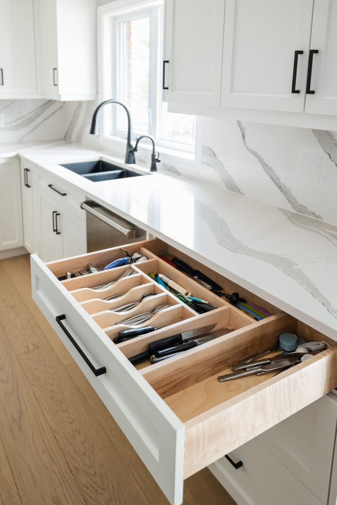 Mid-sized transitional u-shaped light wood floor eat-in kitchen photo in Toronto with an undermount sink, shaker cabinets, white cabinets, quartz countertops, white backsplash, quartz backsplash, stainless steel appliances, an island and white countertops