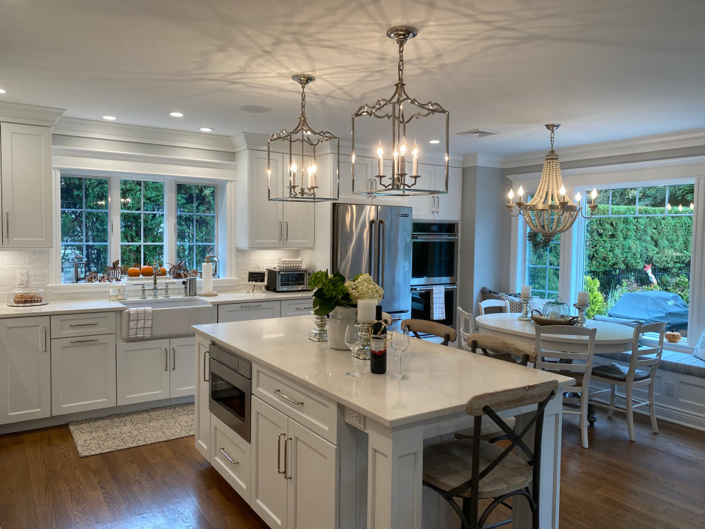 Eat-in kitchen - large traditional l-shaped medium tone wood floor eat-in kitchen idea in New York with a farmhouse sink, shaker cabinets, white cabinets, white backsplash, an island and white countertops