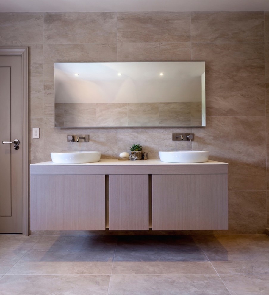 This is an example of a large contemporary master bathroom in West Midlands with flat-panel cabinets, light wood cabinets, a freestanding tub, an open shower, a wall-mount toilet, beige tile, ceramic tile, white walls, ceramic floors, a trough sink and quartzite benchtops.