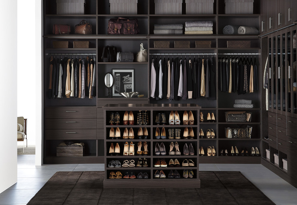 Contemporary gender-neutral walk-in wardrobe in Other with flat-panel cabinets, dark wood cabinets and concrete floors.