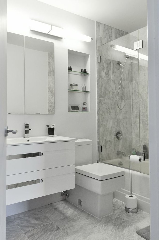 Design ideas for a mid-sized contemporary bathroom in New York with an integrated sink, white cabinets, solid surface benchtops, an alcove tub, an alcove shower, a two-piece toilet, gray tile and marble floors.