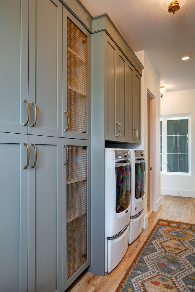 Design ideas for a mid-sized beach style galley utility room in Salt Lake City with shaker cabinets, green cabinets, white walls, medium hardwood floors, a side-by-side washer and dryer and brown floor.