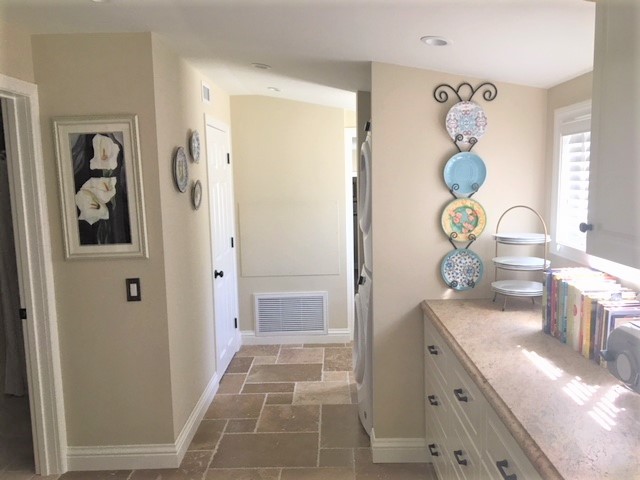 This is an example of a mid-sized traditional galley utility room in Los Angeles with white cabinets, granite benchtops, beige walls, travertine floors, a stacked washer and dryer, beige floor, beige benchtop and raised-panel cabinets.