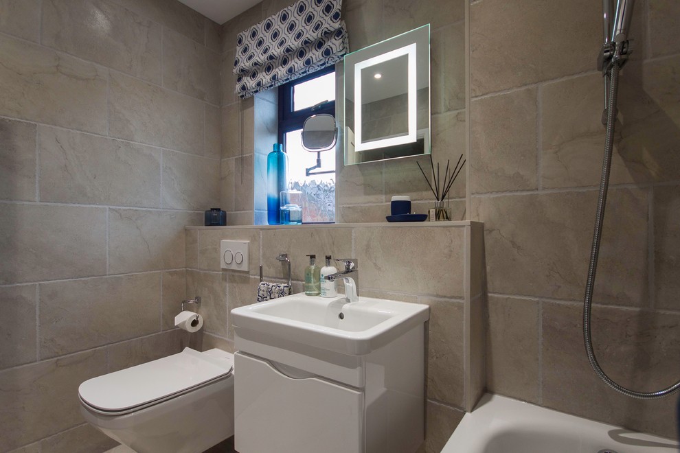 Design ideas for a small contemporary kids bathroom in Buckinghamshire with white cabinets, a drop-in tub, a shower/bathtub combo, a wall-mount toilet, beige tile, porcelain tile, beige walls, ceramic floors and a wall-mount sink.