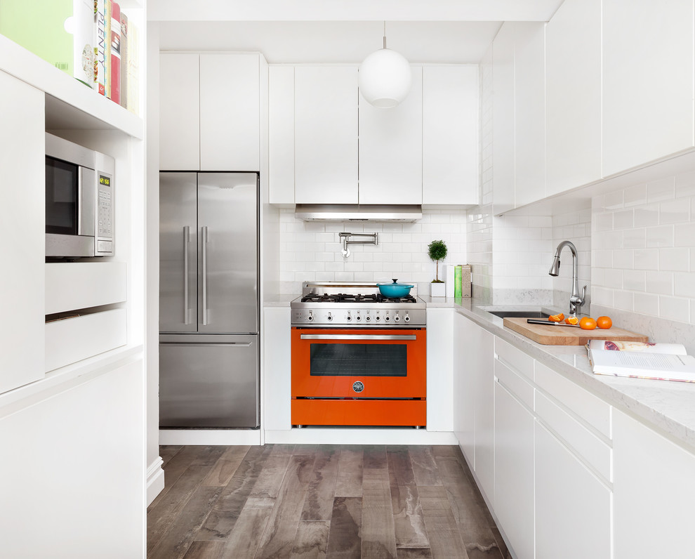 Photo of a small contemporary l-shaped separate kitchen in New York with an undermount sink, flat-panel cabinets, white cabinets, subway tile splashback, coloured appliances, porcelain floors, no island, grey floor, white splashback and white benchtop.