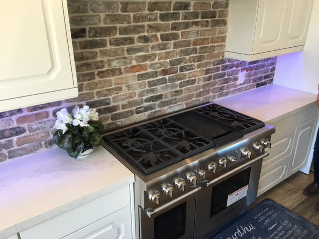 Example of a mid-sized transitional single-wall kitchen design in Austin with a farmhouse sink, raised-panel cabinets, white cabinets, stainless steel appliances and an island