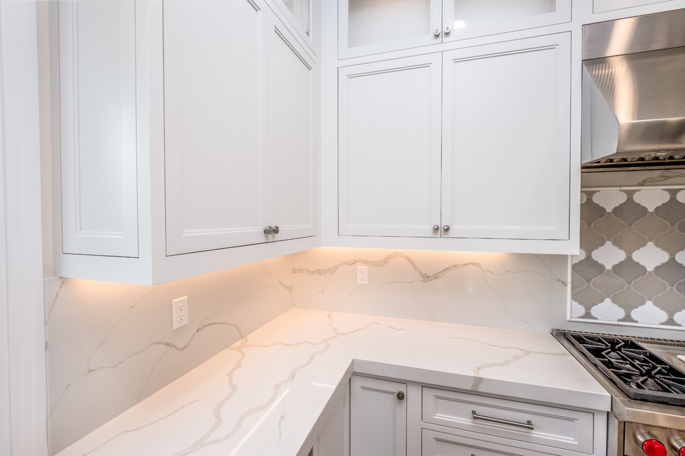 Inspiration for a mid-sized transitional l-shaped porcelain tile and beige floor enclosed kitchen remodel in Orange County with a farmhouse sink, recessed-panel cabinets, white cabinets, quartz countertops, white backsplash, marble backsplash, stainless steel appliances and an island