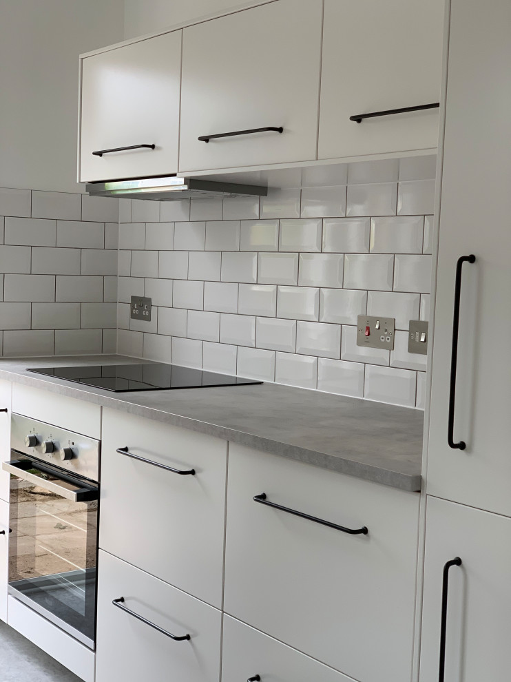Small contemporary galley separate kitchen in Surrey with a double-bowl sink, flat-panel cabinets, white cabinets, laminate benchtops, white splashback, ceramic splashback, stainless steel appliances, vinyl floors, no island, grey floor and grey benchtop.